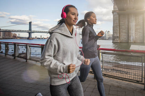 young women jogging on sidewalk by east river - east river audio imagens e fotografias de stock