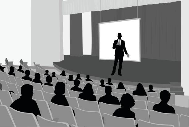 Talent Speaks A man is speaking on stage at a lecture hall.  Attendents are sitting in theatre like seating. lecture hall illustrations stock illustrations