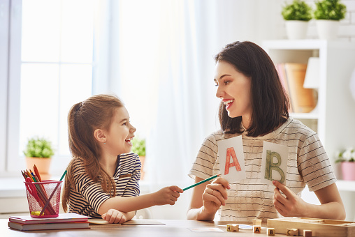 Happy family. Mother and daughter are learning to write. Adult woman teaches child the alphabet.