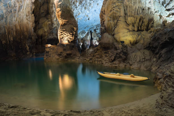 falaise de fleuve et de roche, et bateau touristique d'aviron à l'intérieur de la caverne de phong nha dans le parc national de phong nha-ke bang, un site du patrimoine mondial de l'unesco dans la province de quang binh, vietnam - geological feature cave sedimentary rock limestone photos et images de collection