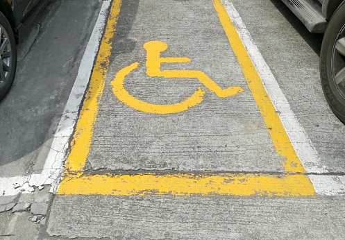 Wheelchair sign on concrete floor indicates parking lot for handicapped people.