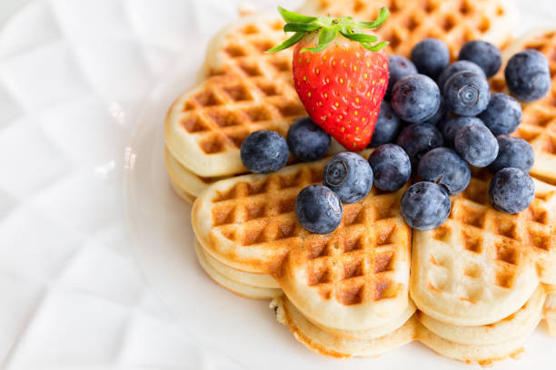 Fresh homemade heart shape waffles with blueberries and strawberry on white plate stock photo