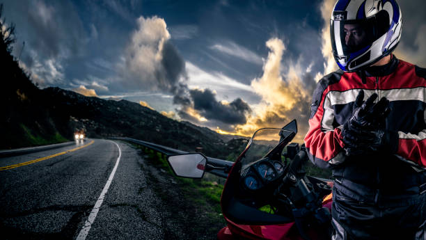 Male motorcyclist wearing protective leather racing suit with a red bike or motorcycle on an open road.  The image is shot in HDR and composite.  The vehicle is cropped to become generic non branded. The image depicts travel and adventure.