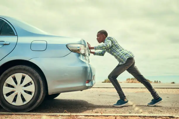 Full length shot of a young man pushing his car along the road after breaking down