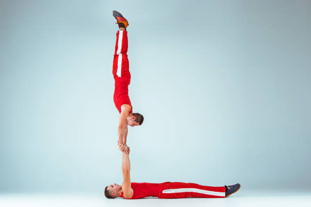 The two gymnastic acrobatic caucasian men on balance pose The two gymnastic acrobatic caucasian men posing in balance posture on gray studio background acrobatic gymnastics stock pictures, royalty-free photos & images