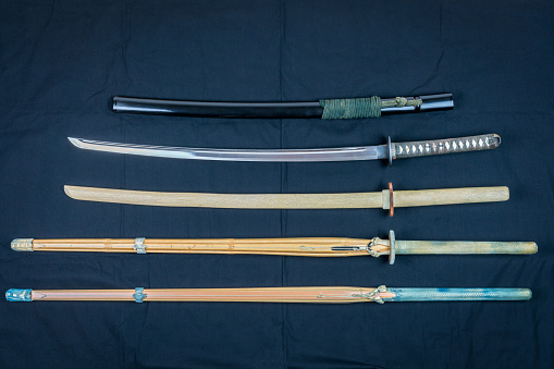 A collection of weapons for training, equipment for Japanese sport Iaido and Kendo. Wood, bamboo and steel sword arranged and displayed on black background.