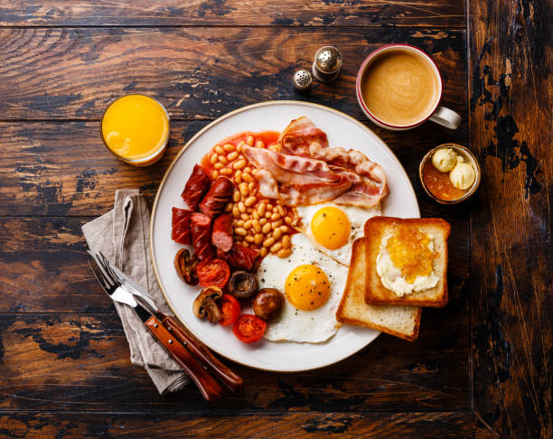 English breakfast Full English breakfast with fried eggs, sausages, bacon, beans, toasts and coffee on wooden background english breakfast stock pictures, royalty-free photos & images