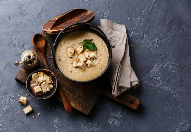 Cream-soup with porcini mushroom with croutons in black iron pot on dark stone background copy space