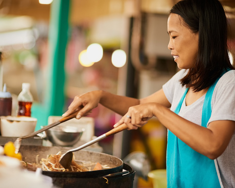 Shot of a happy food vendor preparing a Thai dish at a food market