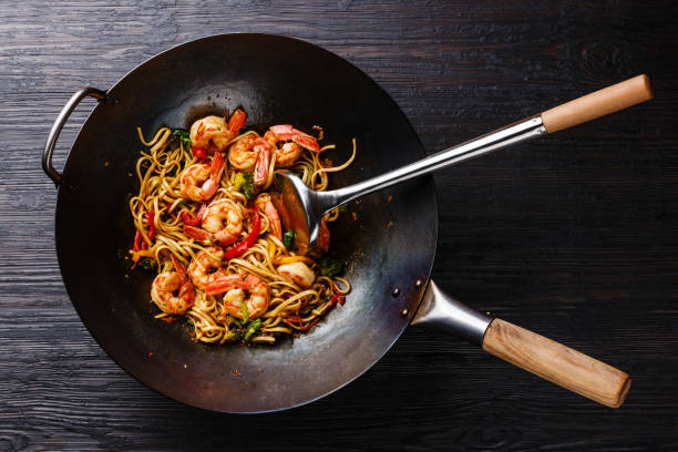 Udon stir-fry noodles with shrimp and vegetables in wok pan Udon stir-fry noodles with shrimp and vegetables in wok pan on black burned wooden background stir fried stock pictures, royalty-free photos & images