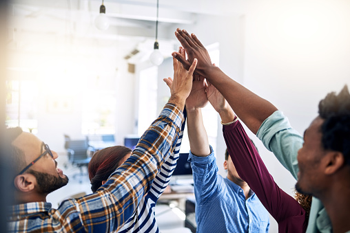 Cropped shot of a team of designers high fiving together  in an office