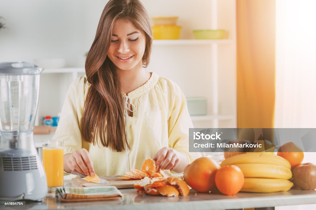 Girl With Fruit Beautiful young woman cutting orange in the kitchen. Adult Stock Photo