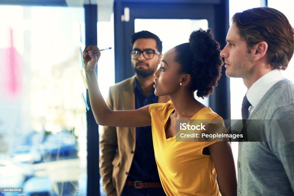 Developing a plan of action Cropped shot of a group of businesspeople brainstorming with notes on a glass wall in an office Teamwork Stock Photo