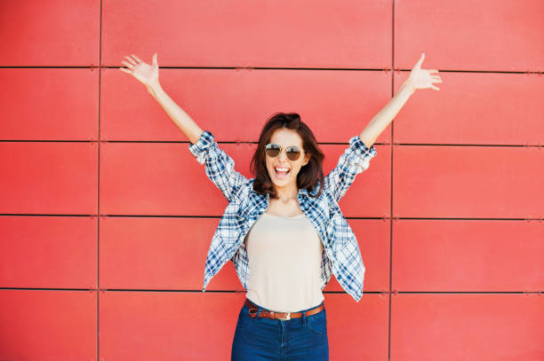 Happy girl with arms raised against red wall