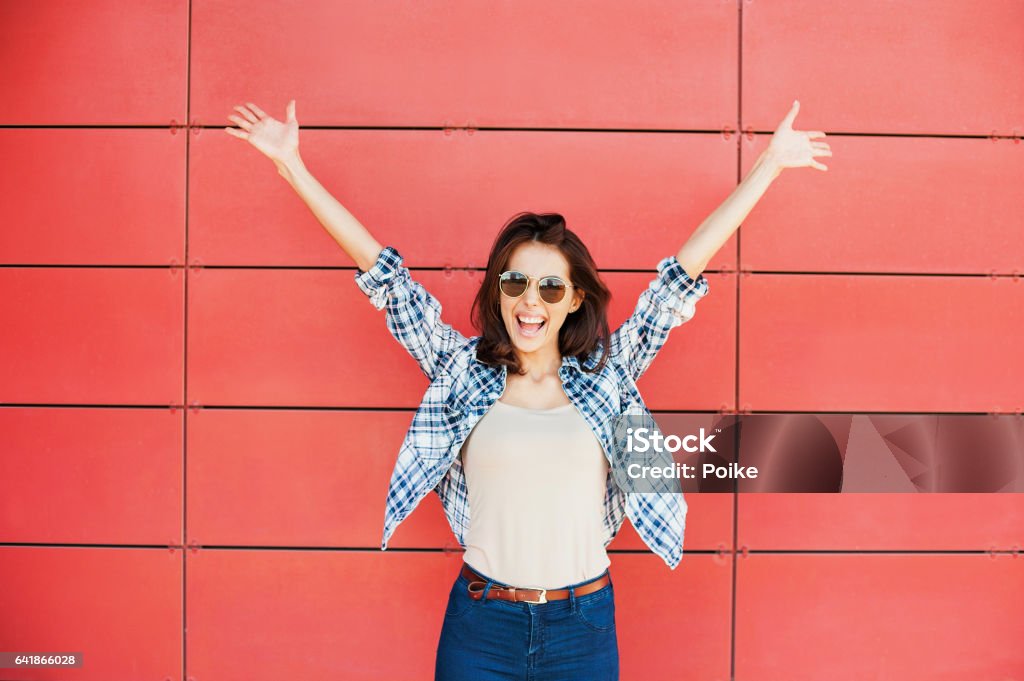 Happy girl with arms raised against red wall Excited happy woman portrait Women Stock Photo