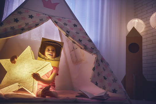 Child in an astronaut costume playing and dreaming of becoming a spacemen. Happy kid plays in tent. Funny lovely girl having fun in children room.