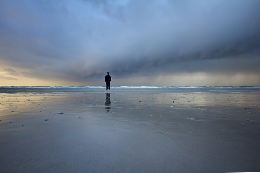29th December 2013, Germany, St. Peter Ording in Schleswig Holstein. Lonely man in a black rain coat is standing in the middle of a stormy rainy cloudy weather in the mudflat of the north sea