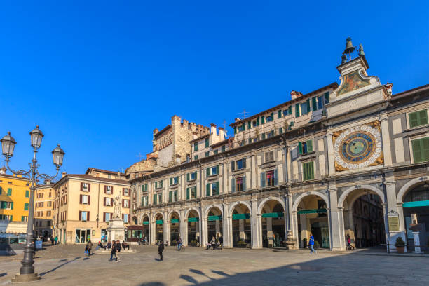 People strolling in Piazza della Loggia, a rectangular square dating from the fifteenth century, bordered by a series of Venetian era buildings including the Loggia, the seat of the City Council of Brescia, and the clock tower. (Lombardy, Italy)