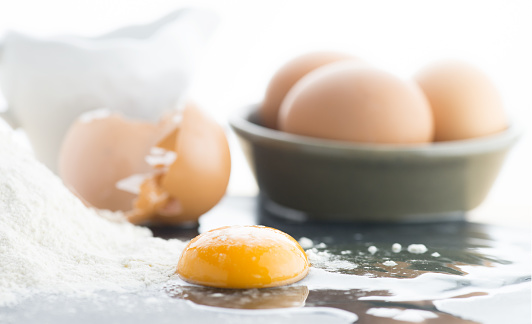 single egg yolk with shell and whole eggs in the background flour to the side shot with a selective focus for copy space