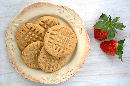 Fresh baked peanut butter cookies with strawberries on rustic white background shot in natural light