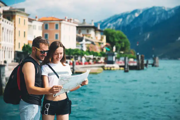 Travel Italy, Europe. Smiling couple in love with a map at Lake Garda with mountains, lake and town on the background. Lake Garda is the largest lake in Italy. Lifestyle, Holidays and Travel Concept.