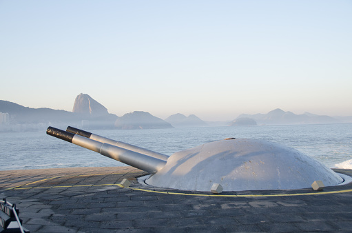 The photo focuses on a double barrel cannon located in Fort Copacabana. The Fort is a military base at the south end of the beach.The base is open to the public and contains the Museu Histórico do Exército (Army Historical Museum) and a coastal defense fort that is the actual Fort Copacabana.
