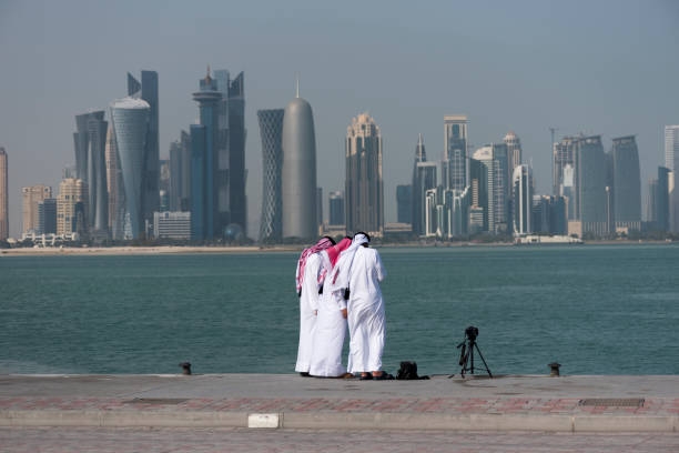 Three high school-aged Qatari boys stand togther while photographing the skyline of Doha, Qatar.
