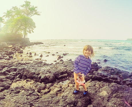 little girl in water gear stands on a rocky coastline in Hawaii