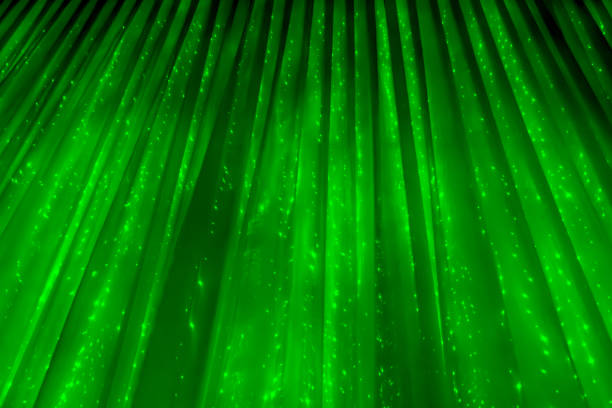 Green abstract background. Curtain with glowing lights. Christmas abstraction. Fabric texture. Waves and creases in hanging fabric. Lights garland through the curtain.