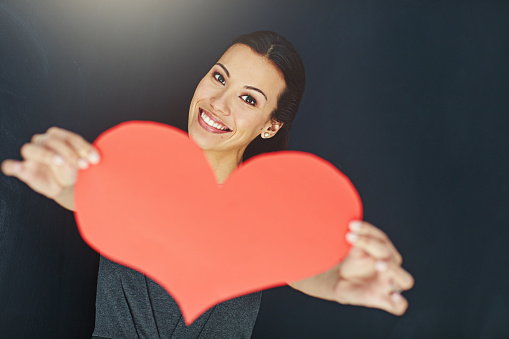 Portrait of a young woman posing with a heart against a gray background