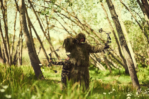 Shot of a father and son in camouflage hunting with bows and arrows in the woods