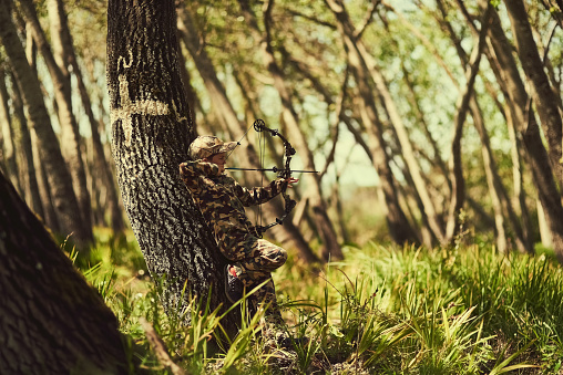 Shot of a cute little boy in camouflage playing with his bow and arrow in the woods