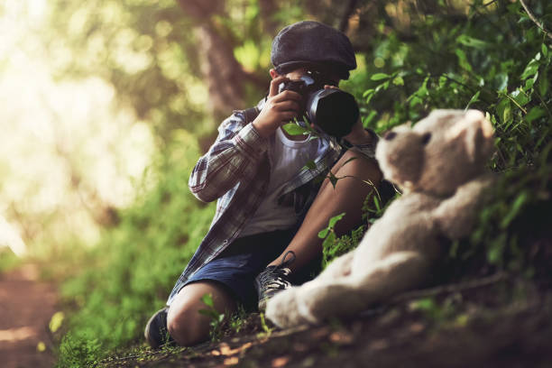 Shot of an unidentifiable young boy using a camera to take photos of his teddy in the woods