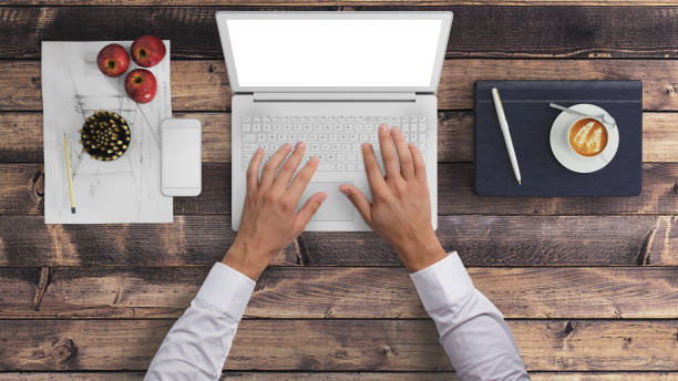 Direct view at hands typing on a laptop.Office desk with laptop, smartphone, coffee, notebook, pencils, and a plant. Blue and white color. copy space. blank screen. render hipster mockup.