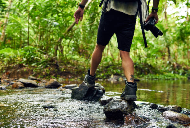 Cropped shot of an unidentifiable hiker crossing a stream while exploring in the woods