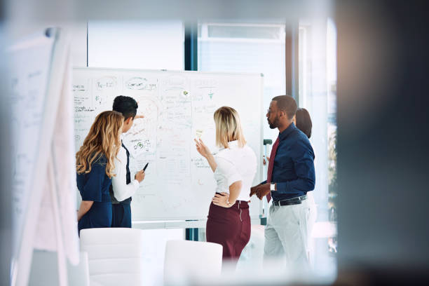 Getting the project moving Cropped shot of a group of businesspeople working together in the office whiteboard stock pictures, royalty-free photos & images