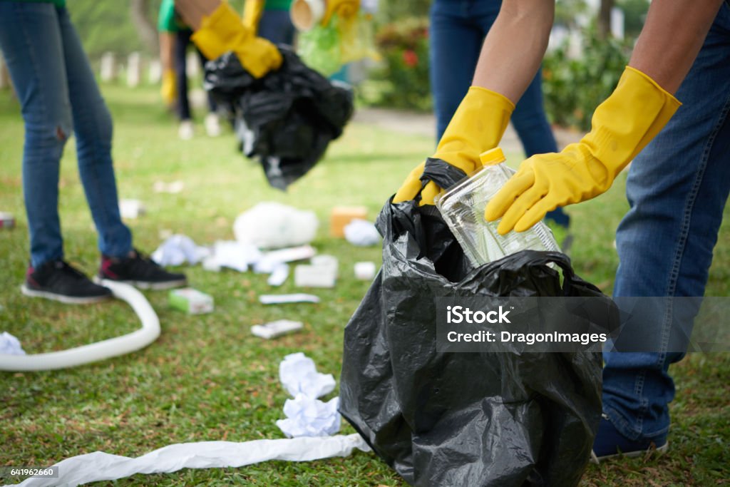 Man in rubber gloves collecting rubbish Male hands in yellow rubber gloves putting household waste into small bin bag Garbage Stock Photo