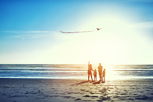 Shot of a family of four watching a kite flying in the sky at the beach.