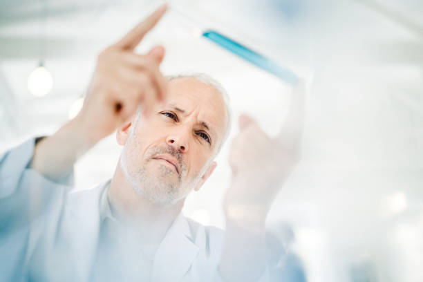 Male doctor analyzing sample in test tube at lab. Low angle view of professional is experimenting. Focus is on scientist.