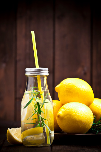 Healthy eating concept: Vertical shot of infused lemon water detox drink in glass bottle with lemon fruit around it on rustic wood table. Copy space left at the top of the frame.  Predominant colors are yellow and brown. DSRL studio photo taken with Canon EOS 5D Mk II and Canon EF 70-200mm f/2.8L IS II USM Telephoto Zoom Lens
