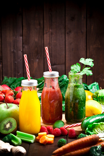 Healthy eating concept: Vertical shot of three detox drinks in glass bottles with fruits and vegetables all around them on rustic wood table. Copy space left at the top of the frame. DSRL studio photo taken with Canon EOS 5D Mk II and Canon EF 70-200mm f/2.8L IS II USM Telephoto Zoom Lens