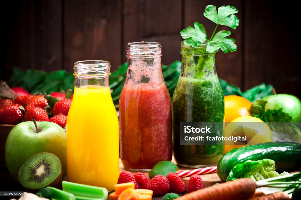 Three fruits and vegetables detox drinks Healthy eating concept: Horizontal shot of three detox drinks in glass bottles with fruits and vegetables all around them on rustic wood table. DSRL studio photo taken with Canon EOS 5D Mk II and Canon EF 70-200mm f/2.8L IS II USM Telephoto Zoom Lens Juice - Drink Stock Photo