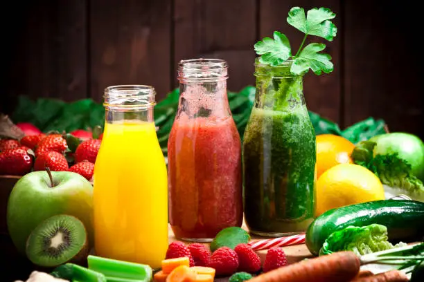 Healthy eating concept: Horizontal shot of three detox drinks in glass bottles with fruits and vegetables all around them on rustic wood table. DSRL studio photo taken with Canon EOS 5D Mk II and Canon EF 70-200mm f/2.8L IS II USM Telephoto Zoom Lens