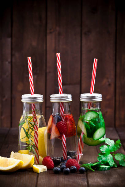 Three fruits and vegetables infused water detox drinks Healthy eating concept: Vertical shot of three infused water detox drinks in glass bottles with fruits and vegetables all around them on rustic wood table. DSRL studio photo taken with Canon EOS 5D Mk II and Canon EF 70-200mm f/2.8L IS II USM Telephoto Zoom Lens infused water stock pictures, royalty-free photos & images