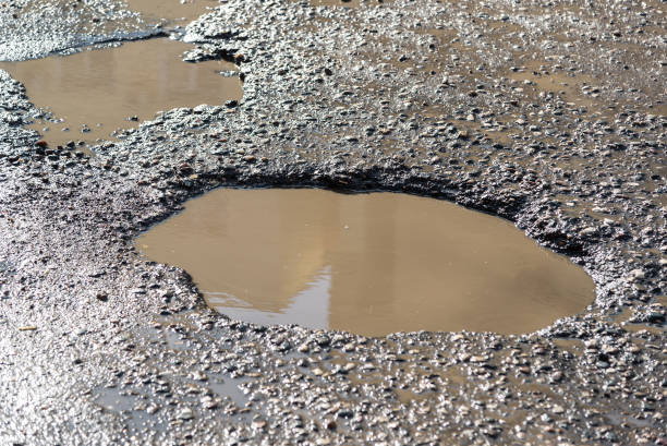 Potholes on asphalt road filled with water stock photo
