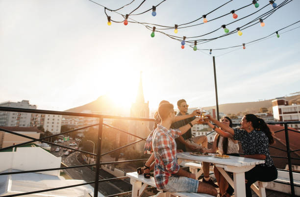 Young people toasting drinks at party Outdoor shot of young people toasting drinks at a rooftop party. Young friends hanging out with drinks. drinking beer stock pictures, royalty-free photos & images