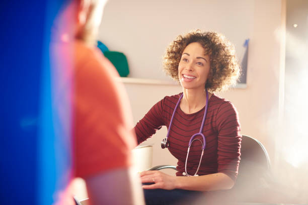 happy female doctor with patient a female doctor sits and chats to a male patient who we see from behind . He is partially obscured by a medical screen. doctor general practitioner stock pictures, royalty-free photos & images