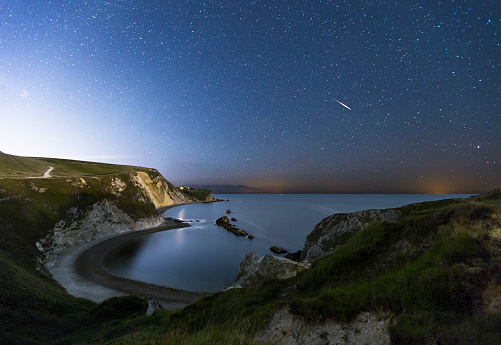 A tranquil night scene on the south coast of Dorset. In the picture you can see Man-O-War Bay. The picture was taken from the east side of the bay. You can see star and a meteor streaking across the sky.
