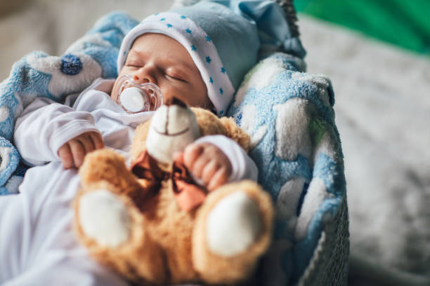 Baby boy wearing diaper and blue towel in white sunny bedroom. Newborn child relaxing in bed after bath or shower. Nursery for children. Textile and bedding for kids. New born kid with toy bear.