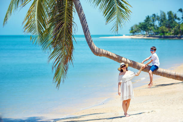 istock Mother and little son at tropical beach sitting on palm tree 642047778